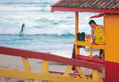 男人在海洋附近的黄色衬衫坐在红色的木头长凳白天
